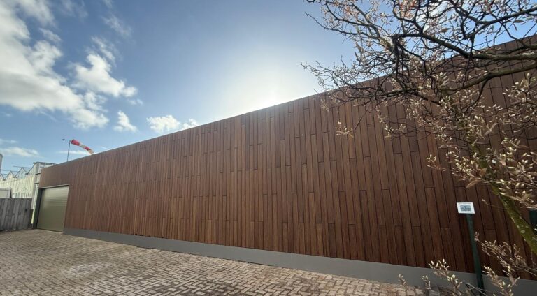 Eindresultaat gevelrenovatie bedrijfspand Maasdijk, voorzien van een duurzame MOSO bamboe gevel, strakke grijze spatrand en een nieuwe overheaddeur.